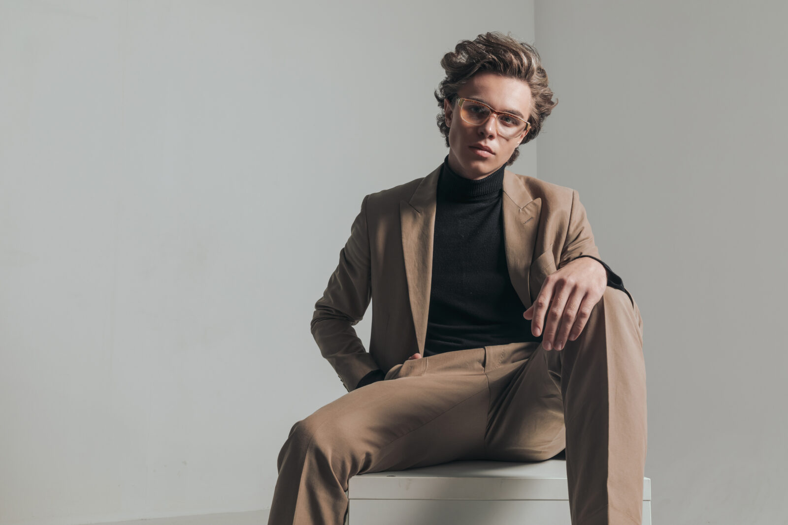 Junger Mann in beigem Anzug posiert im Sitzen.